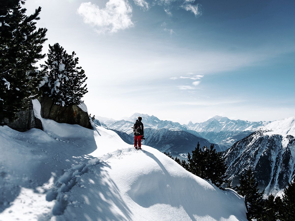 Person standing on a cliff covered with snow overlooking scenery with mountains in the background