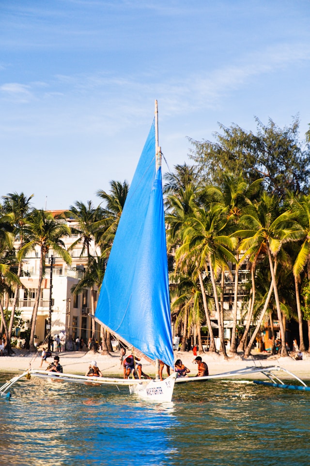 Sunny beach day in Boracay with white sand and blue sailing boats under a clear sky.